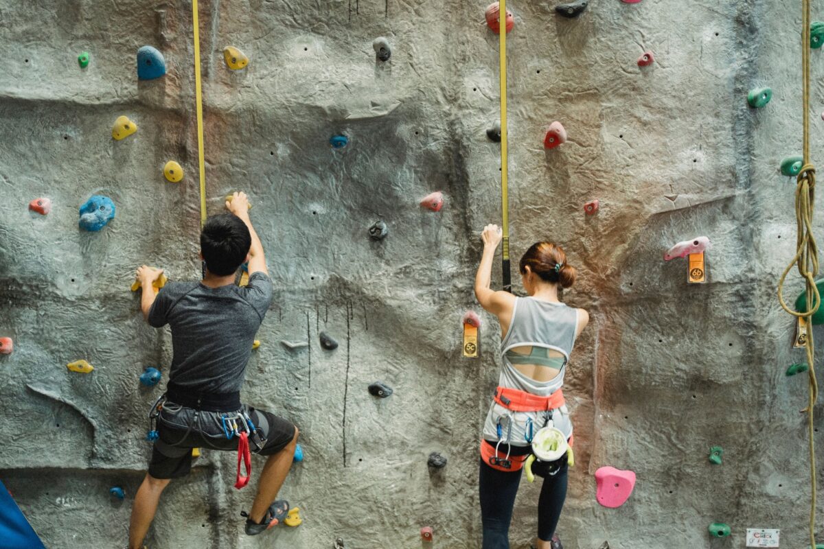 Two adults wearing climbing harnesses on an indoor climbing wall.