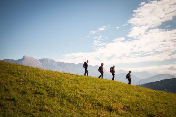 Four walkers with rucksacks crossing a grassy hillside, with mountains in the background.
